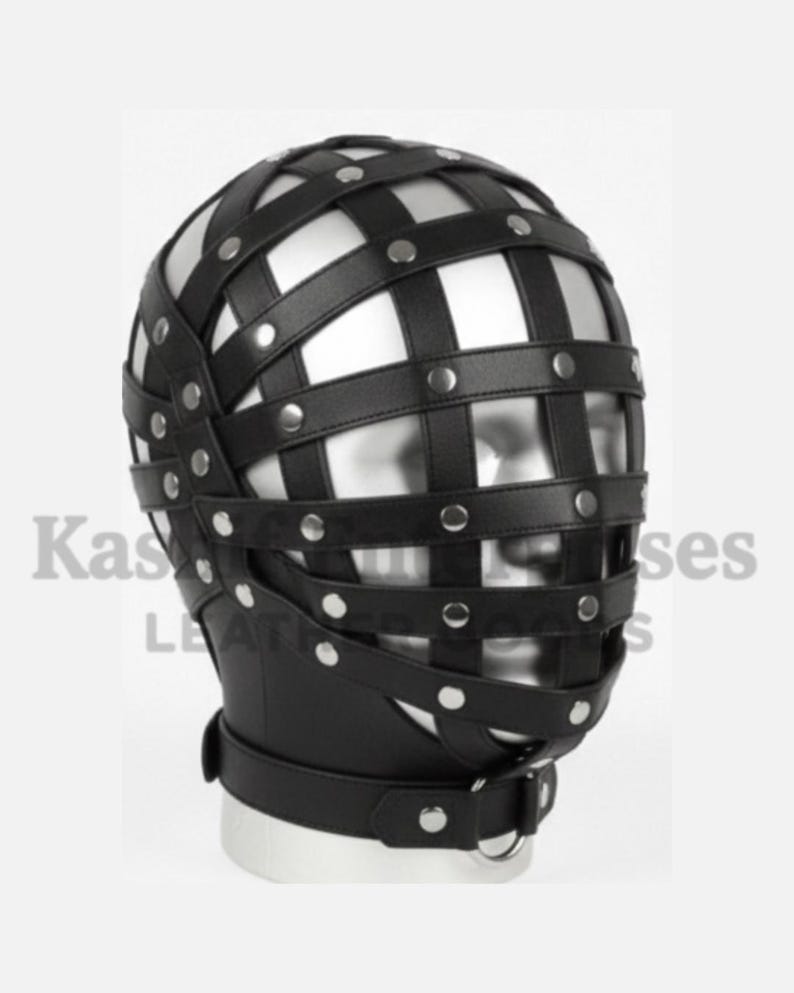 Puede incluir: M&aacute;scara de cabeza de cuero negro con un dise&ntilde;o similar a una jaula. La m&aacute;scara presenta correas horizontales y verticales aseguradas con remaches plateados. Una correa para el cuello con un anillo met&aacute;lico completa el dise&ntilde;o. La m&aacute;scara est&aacute; dise&ntilde;ada para cubrir toda la cabeza.