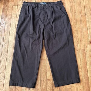 Puede incluir: Pantalones grises oscuros con pliegues, cierre de botón y bolsillos. Los pantalones están hechos de una tela resistente y tienen un corte relajado. El logo de Polo es visible en la parte trasera.