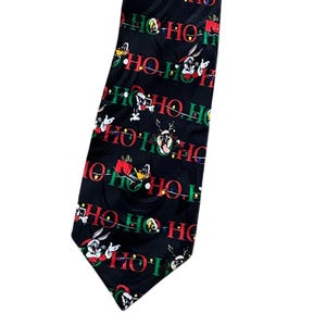 Peut inclure: Cravate noire avec un motif répété de personnages de dessins animés, dont Bugs Bunny et Daffy Duck, avec les mots "HO HO HO" en vert et rouge. Un accessoire festif pour la saison des fêtes.