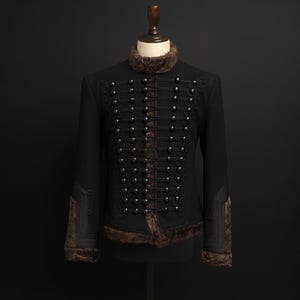 May include: Black jacket with a high collar and decorative silver buttons. The jacket features brown faux fur trim on the collar and cuffs. The front has multiple rows of buttons and decorative cord detailing. The jacket is displayed on a mannequin.