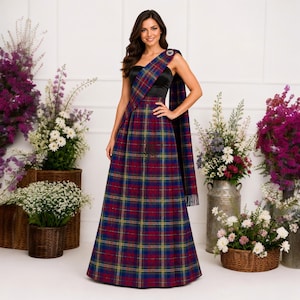 Può includere: Un abito lungo fino ai piedi con corpetto nero senza spalline e una lunga gonna plissettata con motivo tartan a quadri rossi, blu, verdi e gialli. Una fascia in tartan abbinata è drappeggiata su una spalla, fissata da una spilla circolare argentata.