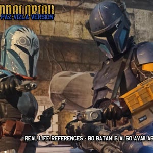 Puede incluir: Dos trajes de armadura completos con cascos y bl&aacute;steres. El traje izquierdo es azul y blanco con marcas de b&uacute;ho. El traje derecho es azul oscuro y amarillo con un bl&aacute;ster pesado. Texto: HEAVY MANDALORIAN PAZ VIZLA VERSION y REDS.