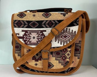 May include: A tan and brown patterned shoulder bag with a brown suede strap and buckle closure. The bag features a geometric design in shades of tan, brown, black, and white. It has a top handle and a flap closure.