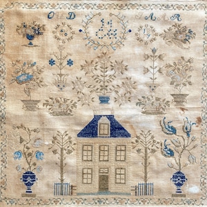 May include: A vintage sampler featuring a detailed embroidered house with a blue roof, surrounded by trees, flowers, and decorative elements. The design incorporates blue and brown thread on a beige background, with the initials "O D" and "J A R".