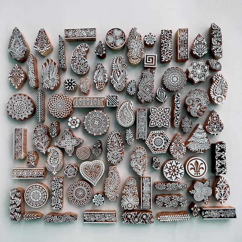 Puede incluir: Una colecci&oacute;n de bloques de impresi&oacute;n de madera tallados intrincadamente con dise&ntilde;os blancos sobre un fondo marr&oacute;n. Los bloques presentan varias formas, incluyendo patrones florales, paisley y geom&eacute;tricos. Estos bloques se utilizan para la impresi&oacute;n textil y la artesan&iacute;a.