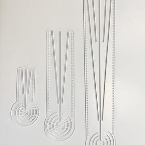 Peut inclure: Trois gabarits en acrylique transparent de différentes tailles. Chaque gabarit présente une base circulaire avec des cercles concentriques, menant à des lignes parallèles. Les bords sont marqués de trous espacés, probablement pour la couture ou l'artisanat. Mesures en centimètres.