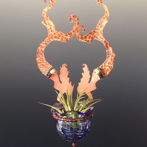 Peut inclure: Un porte-plante en cuivre avec un design décoratif et un pot en verre sphérique. Le porte-plante est orné de perles et le pot est rempli de plantes aériennes.