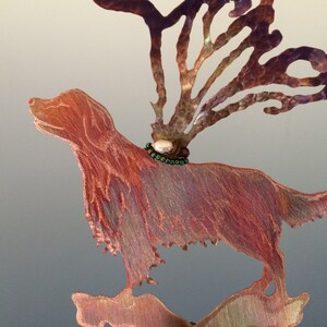 Pode incluir: Uma escultura de metal de cobre de um cão com um colar de pérolas e contas verdes. O cão está em pé sobre uma base com um design de metal de cobre que se assemelha a galhos.