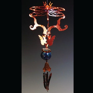 May include: A copper wind chime with a dragonfly, a fairy, and a blue glass orb. The chime is hanging from a copper chain.