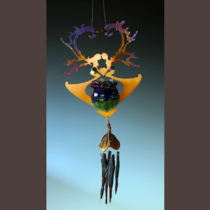 Puede incluir: Un carillón de metal dorado con un diseño abstracto decorativo. El carillón presenta un pequeño recipiente de vidrio redondo azul y verde con una parte superior con cuentas. El carillón cuelga de una cadena de metal dorado.