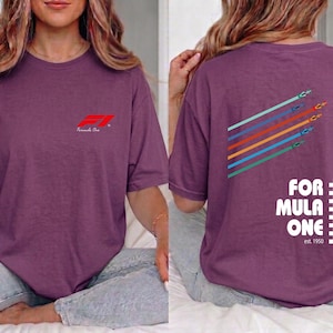 Pu&ograve; includere: Una t-shirt a maniche corte color prugna con un piccolo logo rosso Formula One sul petto. Il retro mostra una grafica di cinque auto da corsa colorate con linee di movimento e il testo Formula One est. 1950 con un bordo a scacchi.