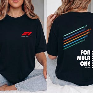 Pu&ograve; includere: Una t-shirt nera a maniche corte con un piccolo logo rosso Formula One sul petto. Il retro mostra una grafica di cinque auto da corsa colorate in linee diagonali con il testo Formula One, un motivo a scacchi e la scritta est. 1950.