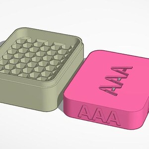 Könnte beinhalten: Ein hellgrüner rechteckiger Behälter mit einem Wabenmuster im Inneren, neben einem rosa Deckel. Der Deckel hat die Buchstaben "AAA" eingraviert. Der Behälter und der Deckel befinden sich auf einer weißen Oberfläche.