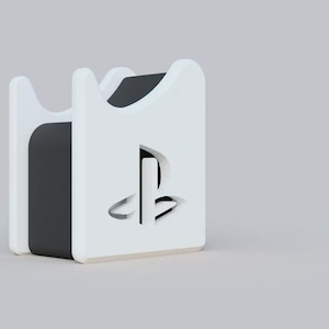 Op de afbeelding: Een wit en zwart PlayStation-consolestandaard. De standaard heeft een rechthoekige vorm met afgeronde randen en een uitsparing van het PlayStation-logo aan de voorkant. De standaard is ontworpen om een console rechtop te houden.