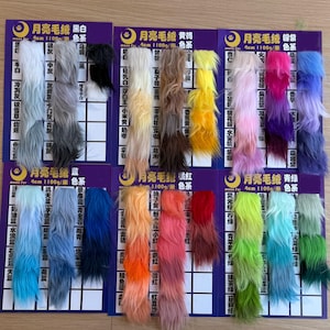 May include: A collection of colorful faux fur samples arranged on purple cards. The samples display a range of colors, including black, white, gray, blue, yellow, pink, and green. Each sample is approximately 4cm in length.