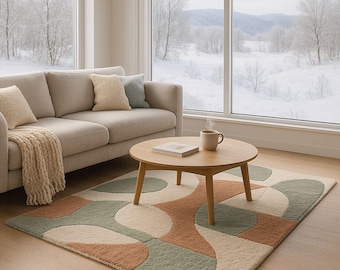 May include: A living room scene featuring a beige sofa with throw pillows and a patterned rug. The rug has a design of overlapping shapes in green, orange, and cream. A wooden coffee table holds a mug and a book. Large windows offer a snowy outdoor view.