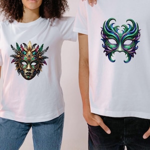 May include: Two white t-shirts featuring colorful Mardi Gras mask designs. One mask is gold, green, and purple with feathers, the other is green, purple, and blue. The shirts are worn by two people, one wearing blue jeans and the other wearing black jeans.
