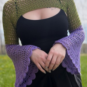 May include: A long-sleeve crochet shrug featuring an olive green open-knit mesh pattern on the upper arms and shoulders, transitioning into wide, flared purple bell sleeves with a scalloped edge at the cuffs, worn over a black tank top.