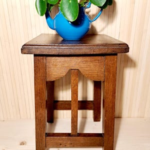 Könnte beinhalten: Kleiner Beistelltisch aus Holz mit quadratischer Platte und vier stabilen Beinen. Eine leuchtend blaue Keramik-Teekanne enthält eine lebendige grüne Pflanze mit runden Blättern. Der Tisch ist aus dunklem Holz gefertigt und hat ein dekoratives Design.