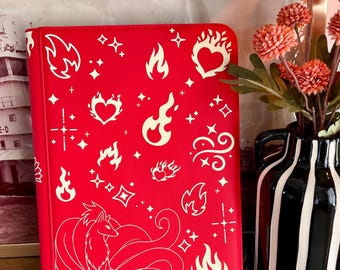 May include: A bright red rectangular binder featuring a white line art pattern of various flame shapes, hearts, and sparkling stars. At the bottom, a large illustration of a multi-tailed fox is depicted in white lines against the red background.