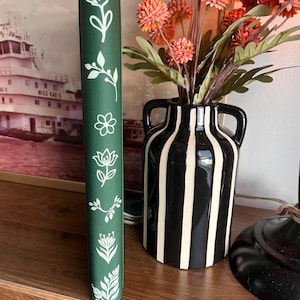May include: A dark green vertical book spine featuring a series of white line-art botanical illustrations including various flowers, leaves, and sprigs arranged in a column along the center of the cover surface.
