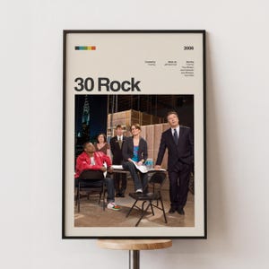 Puede incluir: Un póster enmarcado de la serie de televisión "30 Rock" con fondo beige. El póster presenta una foto del elenco y el título del programa en letras negras grandes. El año "2006" está impreso en la parte superior derecha.