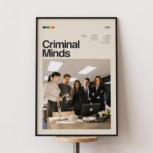 May include: A framed poster for the television show "Criminal Minds" featuring a group of people in an office setting. The poster has the show's title in large, bold letters, with the year 2005 displayed at the top. The poster is in a black frame.