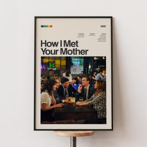 Puede incluir: Un póster enmarcado de la serie de televisión "How I Met Your Mother" con un marco negro. El póster presenta el título del programa, una escena de bar colorida y el año 2005. El póster se muestra en un soporte de madera.