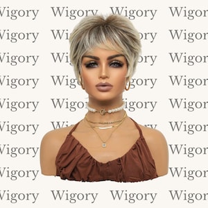 Könnte beinhalten: Ein Schaufensterpuppenkopf mit einer kurzen, blonden Perücke mit dunklen Ansätzen und einem Seitenscheitel. Die Schaufensterpuppe trägt ein braunes Neckholder-Top und mehrere goldene Halsketten. Der Hintergrund ist ein sich wiederholendes Muster des Wortes "Wigory".