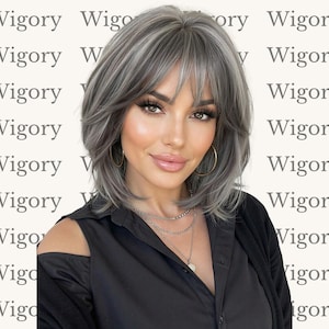 May include: A woman with a layered, shoulder-length wig in shades of gray and silver. The wig has bangs and is styled with a slight wave. She is wearing a black off-the-shoulder top and gold hoop earrings. The background has the word "Wigory" repeated.