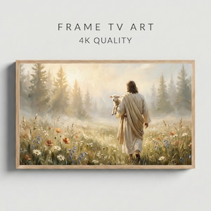 May include: A framed print with the text "FRAME TV ART 4K QUALITY" depicts a person in a cream-colored robe carrying a lamb through a field of wildflowers. The artwork has a soft, painterly style with a light brown wooden frame.