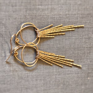 May include: Gold hoop earrings with a fringe of thin, textured metal strands hanging from the bottom.