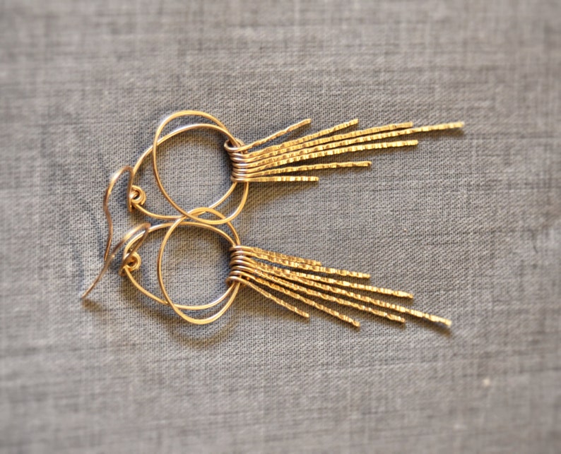 May include: Gold hoop earrings with a fringe of thin, textured metal strands hanging from the bottom.