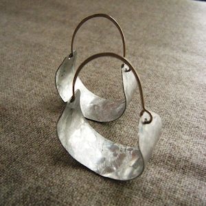 May include: A pair of silver hoop earrings with a hammered texture. The hoops are made of metal and have a simple, modern design.