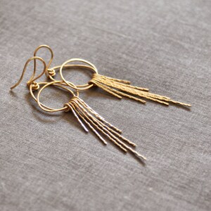 May include: A pair of gold hoop earrings with a dangling fringe of textured metal strands.