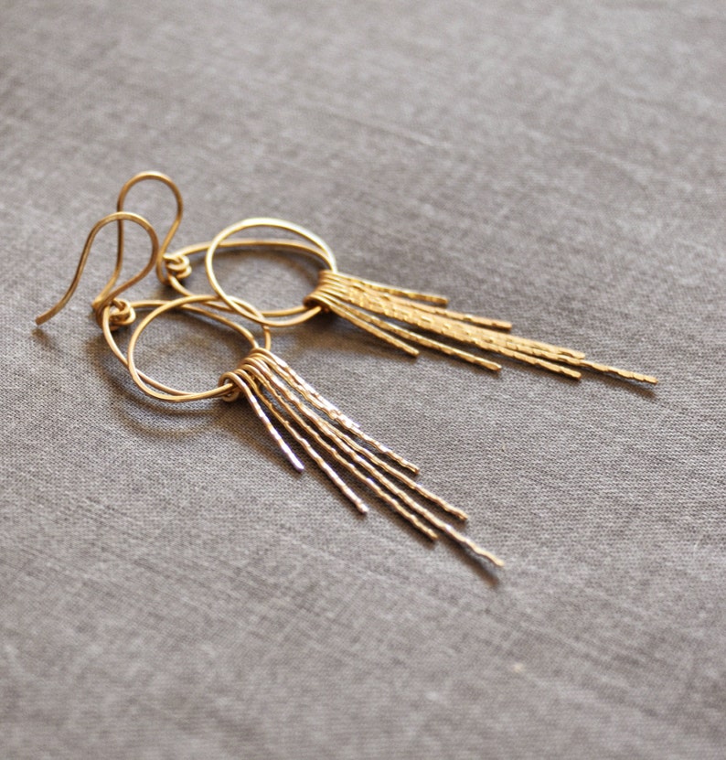 May include: A pair of gold hoop earrings with a dangling fringe of textured metal strands.