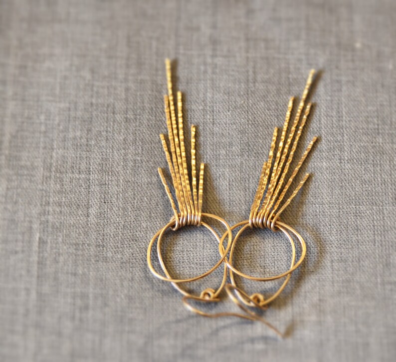 May include: Gold hoop earrings with a fringe of textured metal strands hanging from the bottom.