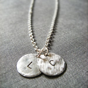May include: A silver chain necklace with two round pendants, each with a letter stamped on them. The letters are "L" and "C".