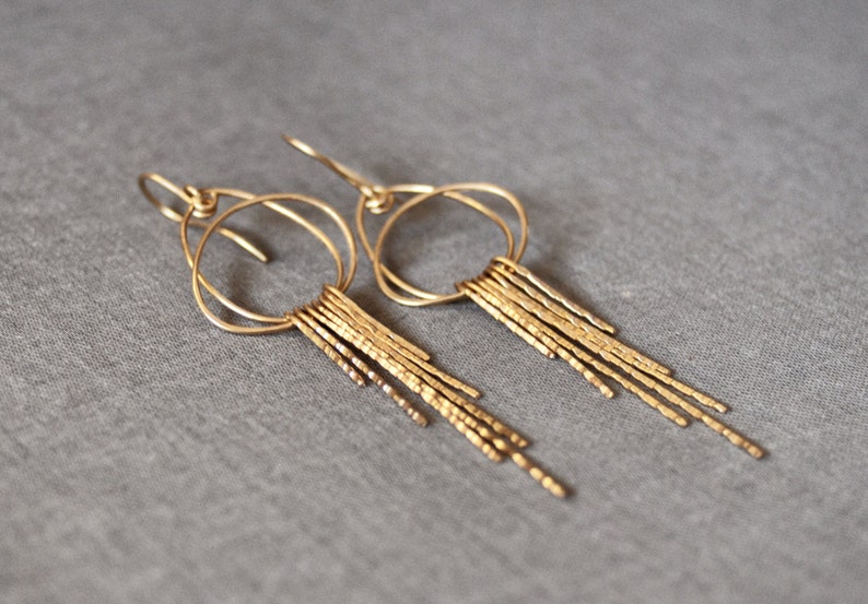 May include: Gold dangle earrings with a circle design and a fringe of textured metal strands.