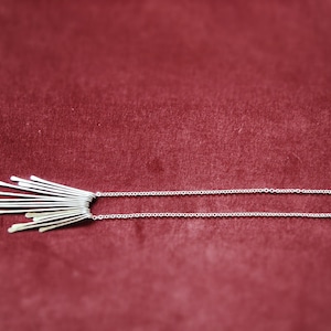 May include: A silver necklace with a delicate chain and a pendant made of multiple thin, silver bars arranged in a fan shape.