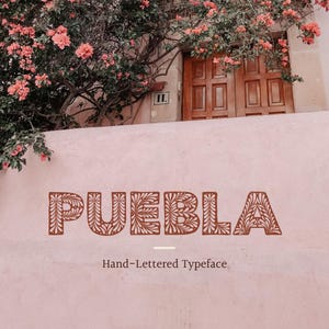 May include: The word "PUEBLA" in a decorative, brown, hand-lettered typeface, with floral-like patterns, is displayed on a pink wall. Below, the text reads "Hand-Lettered Typeface." The background includes a wooden door, pink flowers, and greenery.