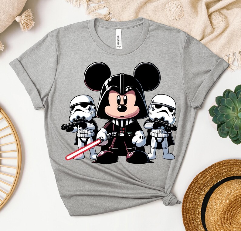 K&ouml;nnte beinhalten: Graues T-Shirt mit einer Cartoon-Illustration von Mickey Mouse als Darth Vader, der ein rotes Lichtschwert h&auml;lt, flankiert von zwei Sturmtruppen. Das Design ist im Cartoon-Stil gehalten, mit kr&auml;ftigen Linien und leuchtenden Farben. Das T-Shirt hat einen Rundhalsausschnitt und kurze &Auml;rmel.