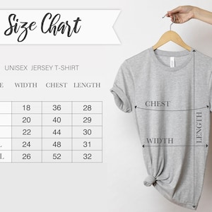 May include: A light grey unisex jersey t-shirt displayed on a wooden hanger. The image includes a size chart with measurements for width, chest, and length in inches. The chart lists sizes S, M, L, XL, and 2XL.