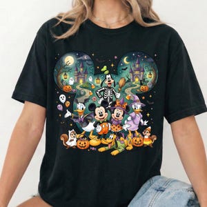 K&ouml;nnte beinhalten: Ein schwarzes T-Shirt mit einer gro&szlig;en Grafik von Disney-Figuren in Halloween-Kost&uuml;men, darunter Mickey, Minnie, Donald, Daisy, Goofy und Pluto. Das Design befindet sich in einer Mickey-Maus-Ohr-Silhouette mit einer gruseligen Schlosskulisse.
