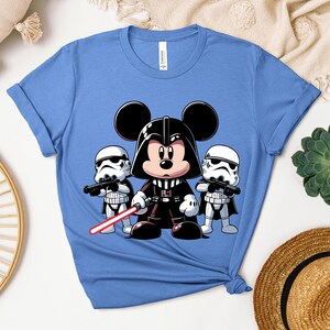 K&ouml;nnte beinhalten: Hellblaues T-Shirt mit einer Cartoon-Illustration von Mickey Mouse als Darth Vader, der ein rotes Lichtschwert h&auml;lt, flankiert von zwei Sturmtrupplern. Das T-Shirt besteht aus einem weichen Material und hat hochgekrempelte &Auml;rmel.