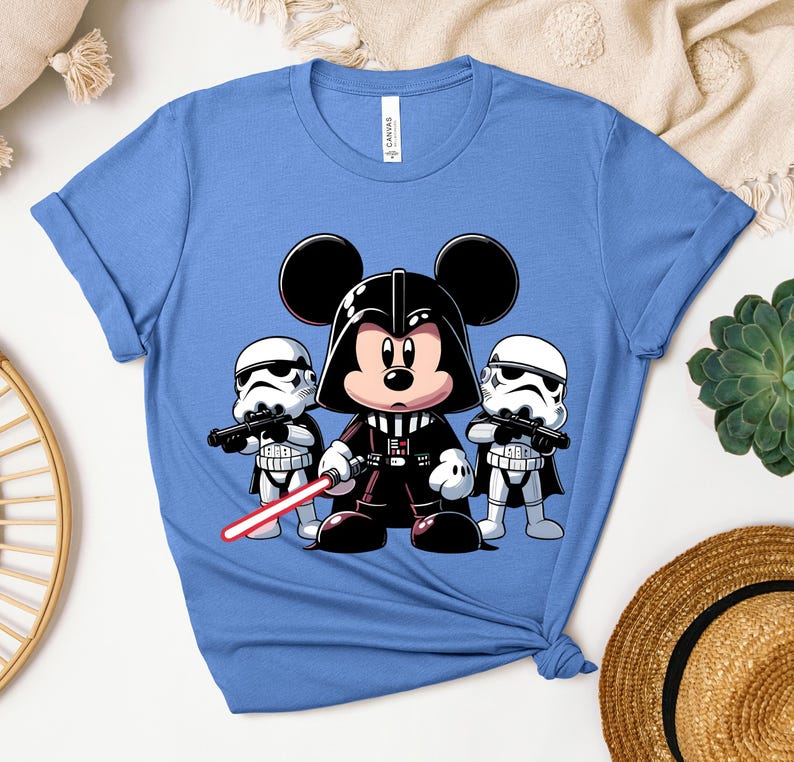 K&ouml;nnte beinhalten: Hellblaues T-Shirt mit einer Cartoon-Illustration von Mickey Mouse als Darth Vader, der ein rotes Lichtschwert h&auml;lt, flankiert von zwei Sturmtrupplern. Das T-Shirt besteht aus einem weichen Material und hat hochgekrempelte &Auml;rmel.