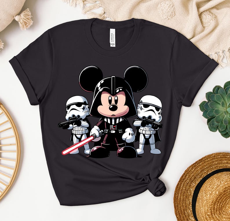 K&ouml;nnte beinhalten: Schwarzes T-Shirt mit einer Cartoon-Illustration von Mickey Mouse als Darth Vader, der ein rotes Lichtschwert h&auml;lt, flankiert von zwei Sturmtruppen. Ein lustiges Design, das Disney- und Star Wars-Themen kombiniert.