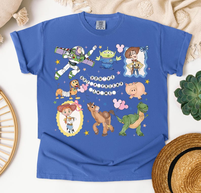 May include: Blue t-shirt featuring cartoon characters from a popular animated film. The design includes Buzz Lightyear, Woody, an alien, Jessie, Hamm, Rex, and Bullseye, with the text "You've Got a Friend in Me."