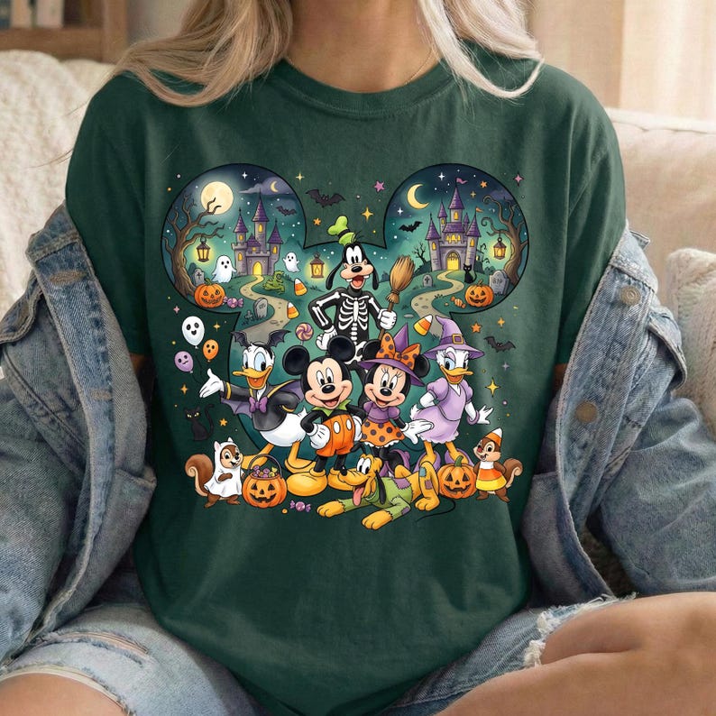 K&ouml;nnte beinhalten: Ein dunkelgr&uuml;nes T-Shirt mit einer gro&szlig;en Grafik von Zeichentrickfiguren in Halloween-Kost&uuml;men. Das Design ist in Form einer Maus-Kopf-Silhouette gehalten und zeigt ein Spukschloss, K&uuml;rbisse, Geister, Flederm&auml;use und Sterne in einer Nachtszene.
