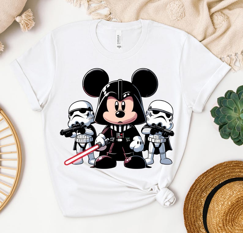 K&ouml;nnte beinhalten: Wei&szlig;es T-Shirt mit einer Cartoon-Illustration von Mickey Mouse als Darth Vader, flankiert von zwei Sturmtruppen. Mickey h&auml;lt ein rotes Lichtschwert. Das Design ist eine spielerische Mischung aus Disney und Star Wars.